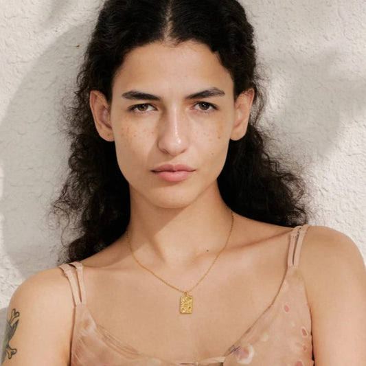 Woman wearing a gold necklace with a pendant against a neutral background
