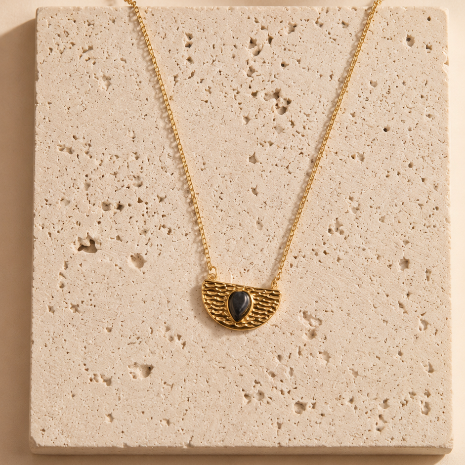 Gold necklace with a pendant on a textured beige surface